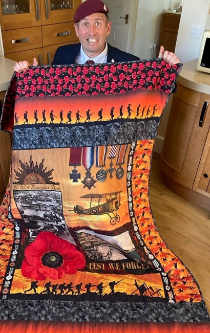 Ben Parkinson MBE holding a handmade remembrance quilt featuring poppies, military medals and First World War imagery.